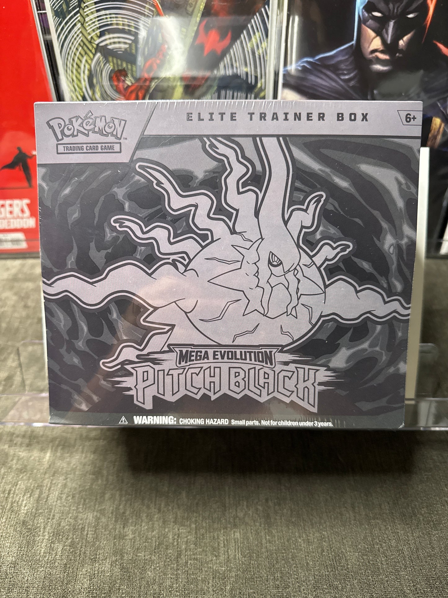 A sealed Pokémon Elite Trainer Box for Pitch Black from the 2024 TCG season, featuring a black and white graphic of Pitch Black on the front, photographed on a gray fabric surface.