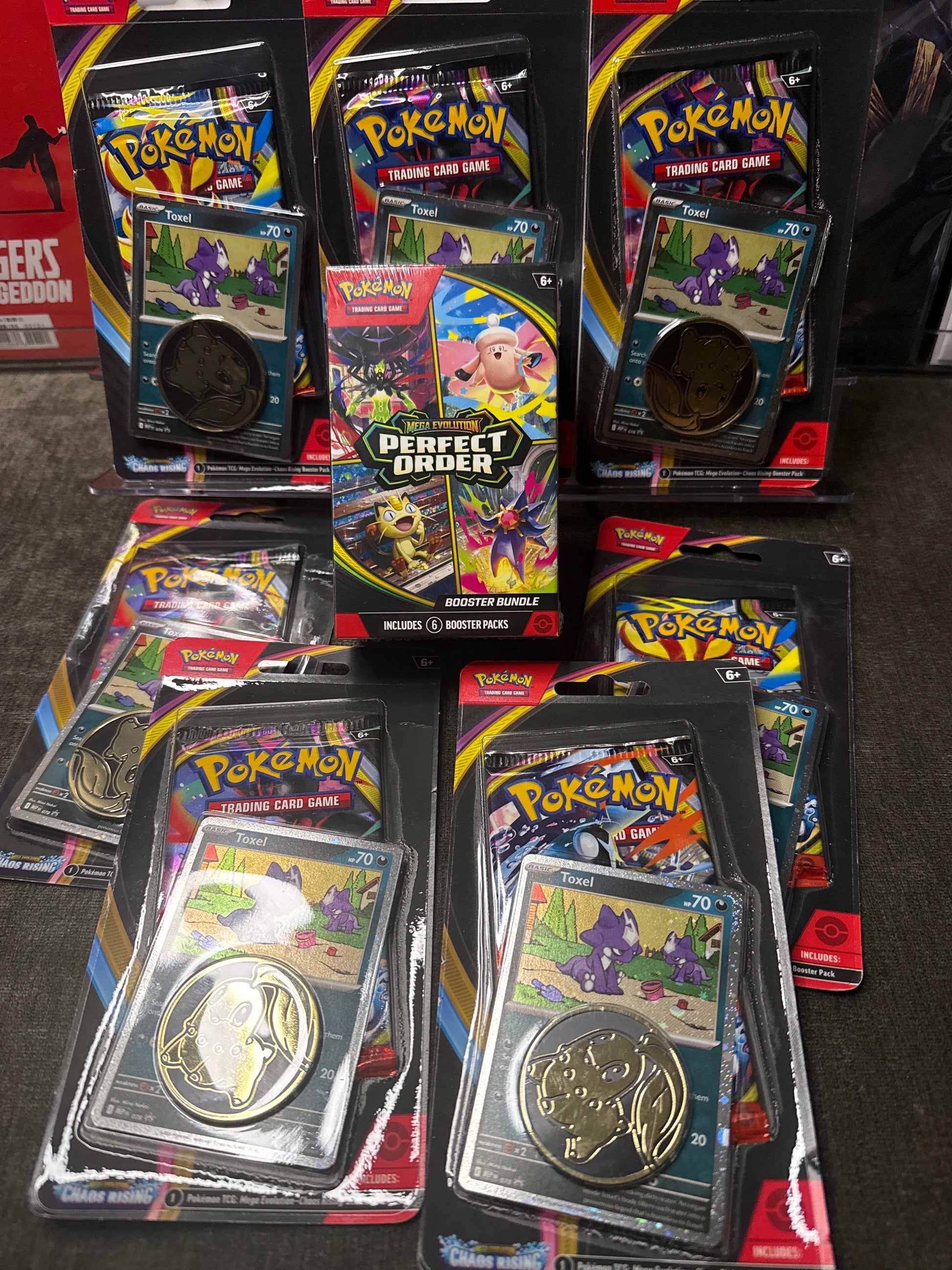 Six packaged Pokémon Perfect 5 Star Cards sets arranged on a dark carpeted floor. Each set is in its original black blister packaging with colorful card inserts and a gold-colored coin featuring the corresponding Pokémon logo.